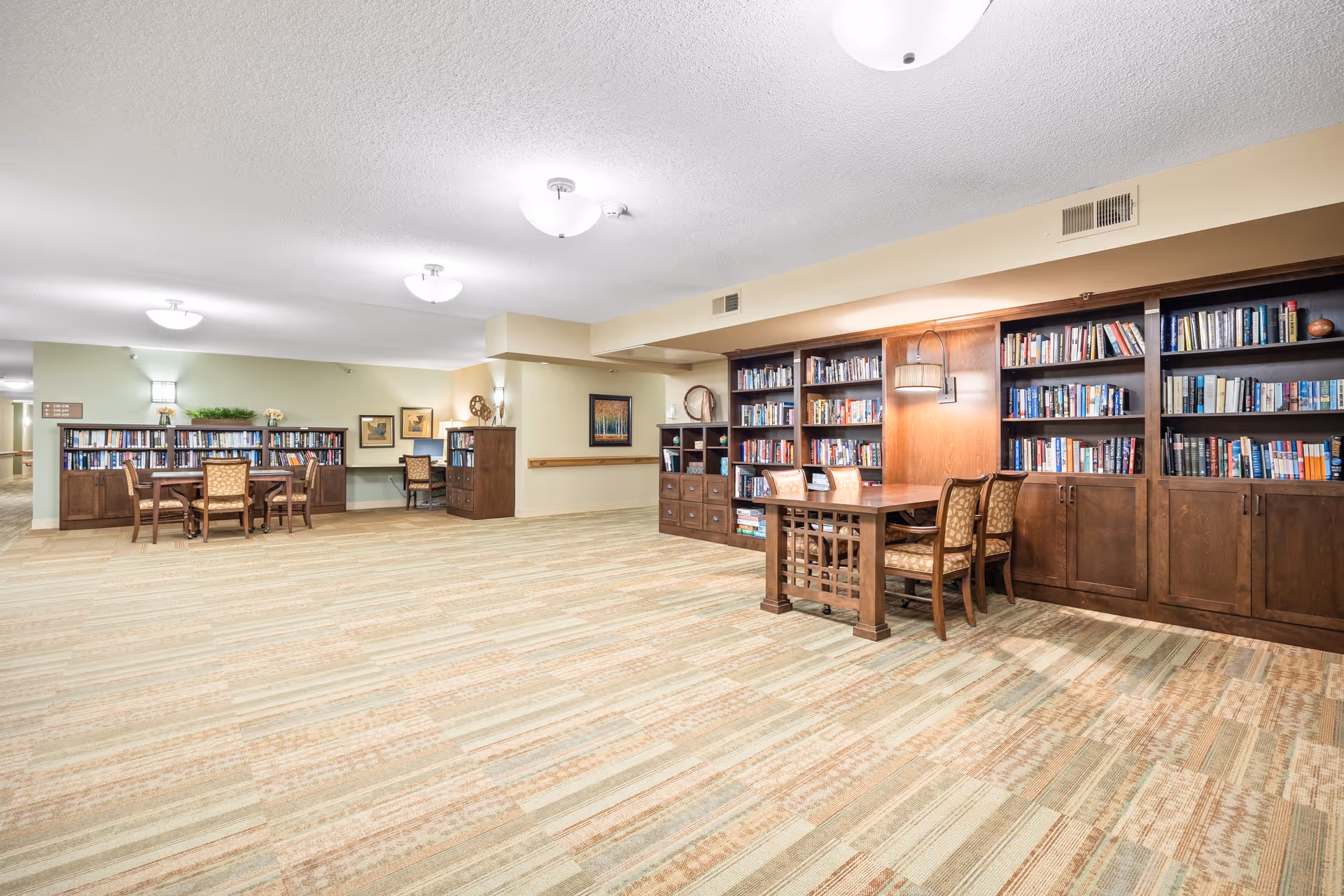 Spacious senior living community library/lounge with built-in bookshelves, tables, and chairs.