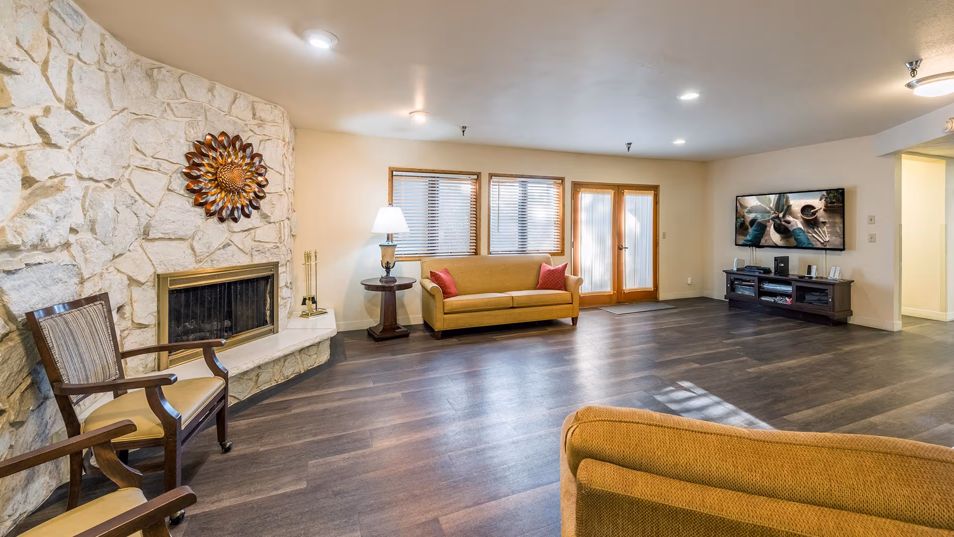 Spacious communal living room with a stone fireplace, seating, wood-look floors, and a wall-mounted TV.