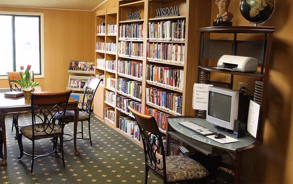 Small communal library/reading room with bookshelves, a table and chairs, and a computer workstation.
