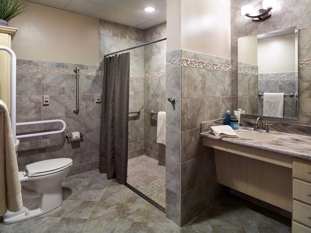 Accessible bathroom with a toilet, grab bars, roll-in shower with curtain, sink and mirror.