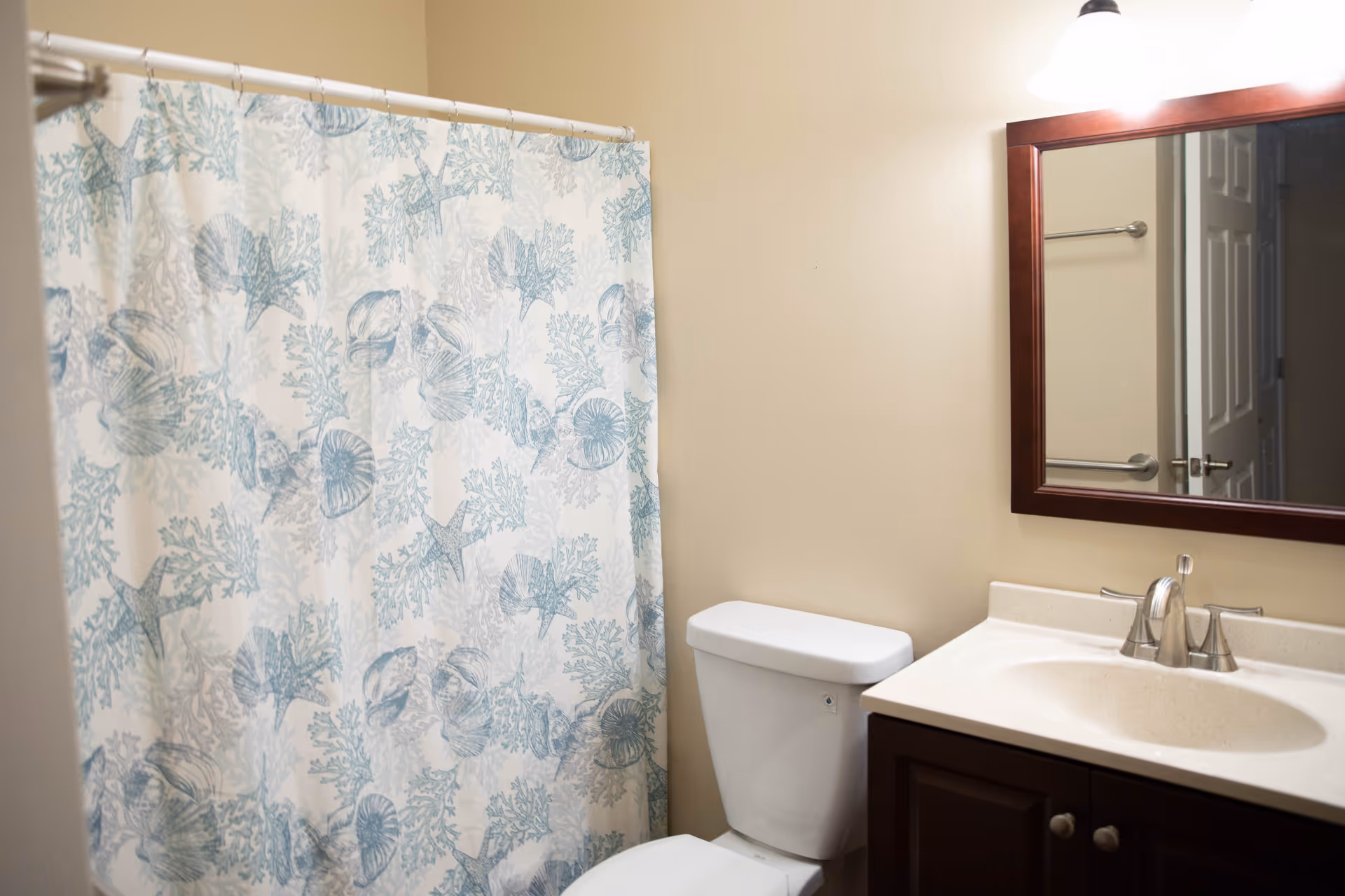 Bathroom with a seashell-patterned shower curtain, toilet, sink vanity, and mirror.