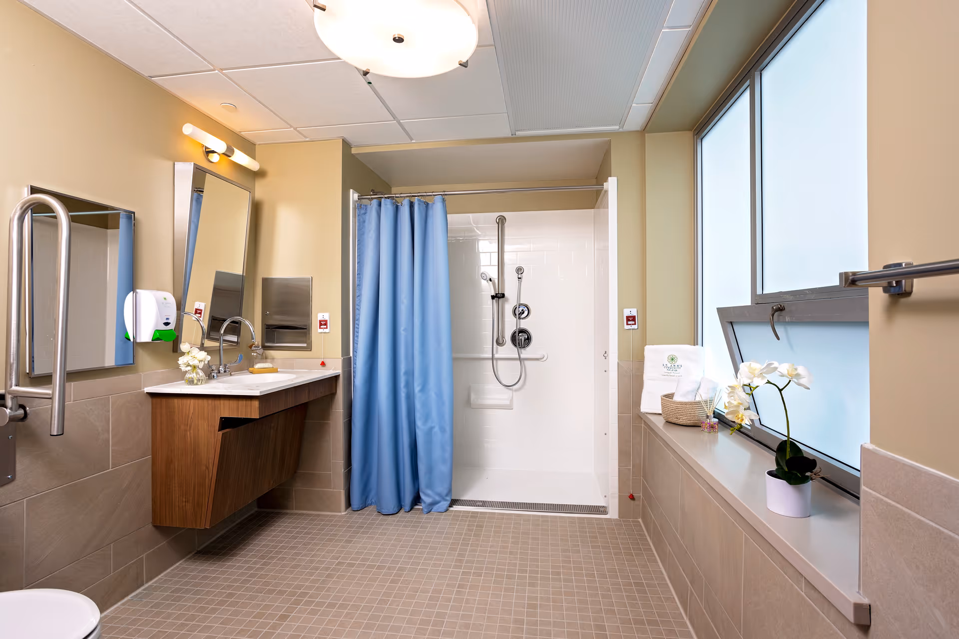 Accessible bathroom with a walk-in shower behind a blue curtain, floating vanity, grab bars, and frosted windows.