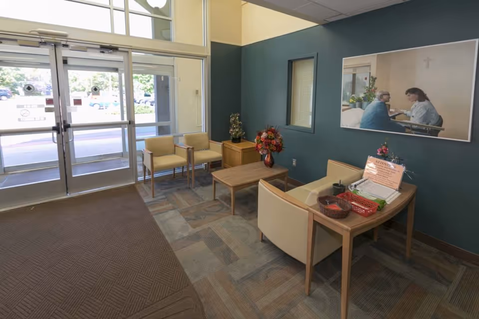 Entrance lobby with glass double doors, chairs, small tables, and floral decorations.