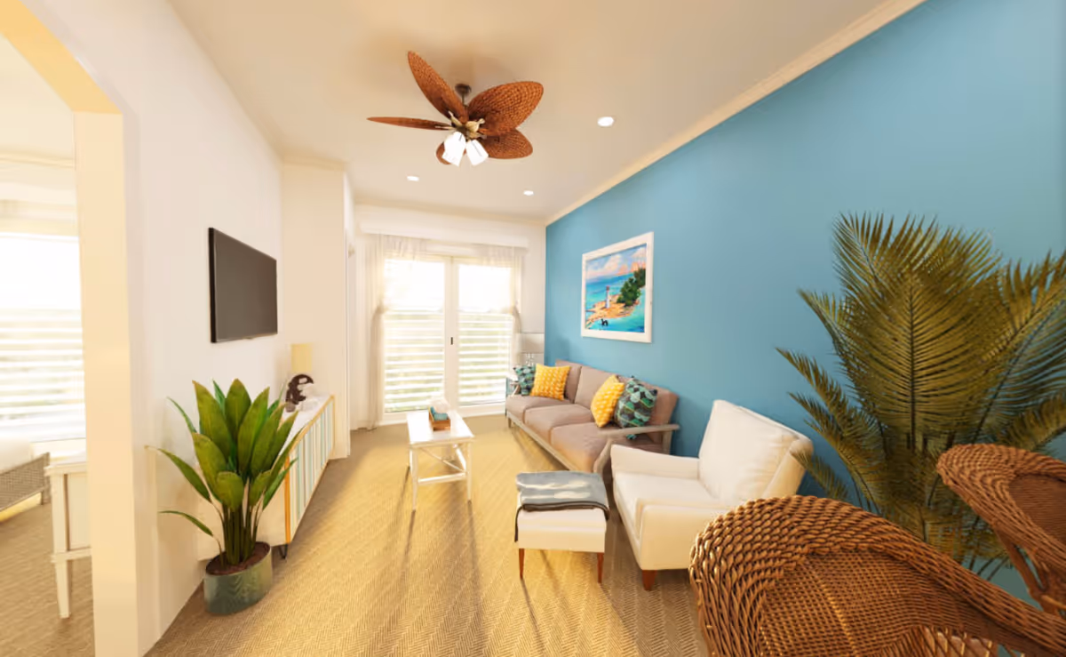 A bright and cozy living room with a blue accent wall, a beige sofa with colorful pillows, a white armchair with a matching ottoman, a white coffee table, a large green potted plant, a wall-mounted flat-screen TV, and a ceiling fan with woven blades. Natural light enters through large windows with sheer curtains.