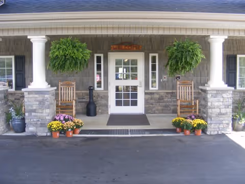 Mitchell House entrance with columns, stone exterior, a Welcome sign, chairs, and potted flowers