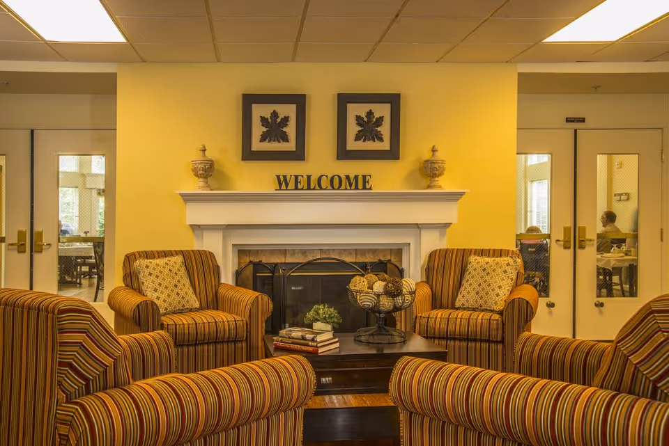 Cozy seating area with striped armchairs arranged around a coffee table in front of a fireplace topped by a 'WELCOME' sign.