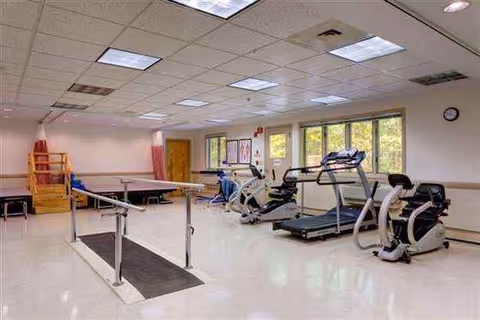 Rehabilitation gym with treadmills, bikes, and parallel bars in a bright room.
