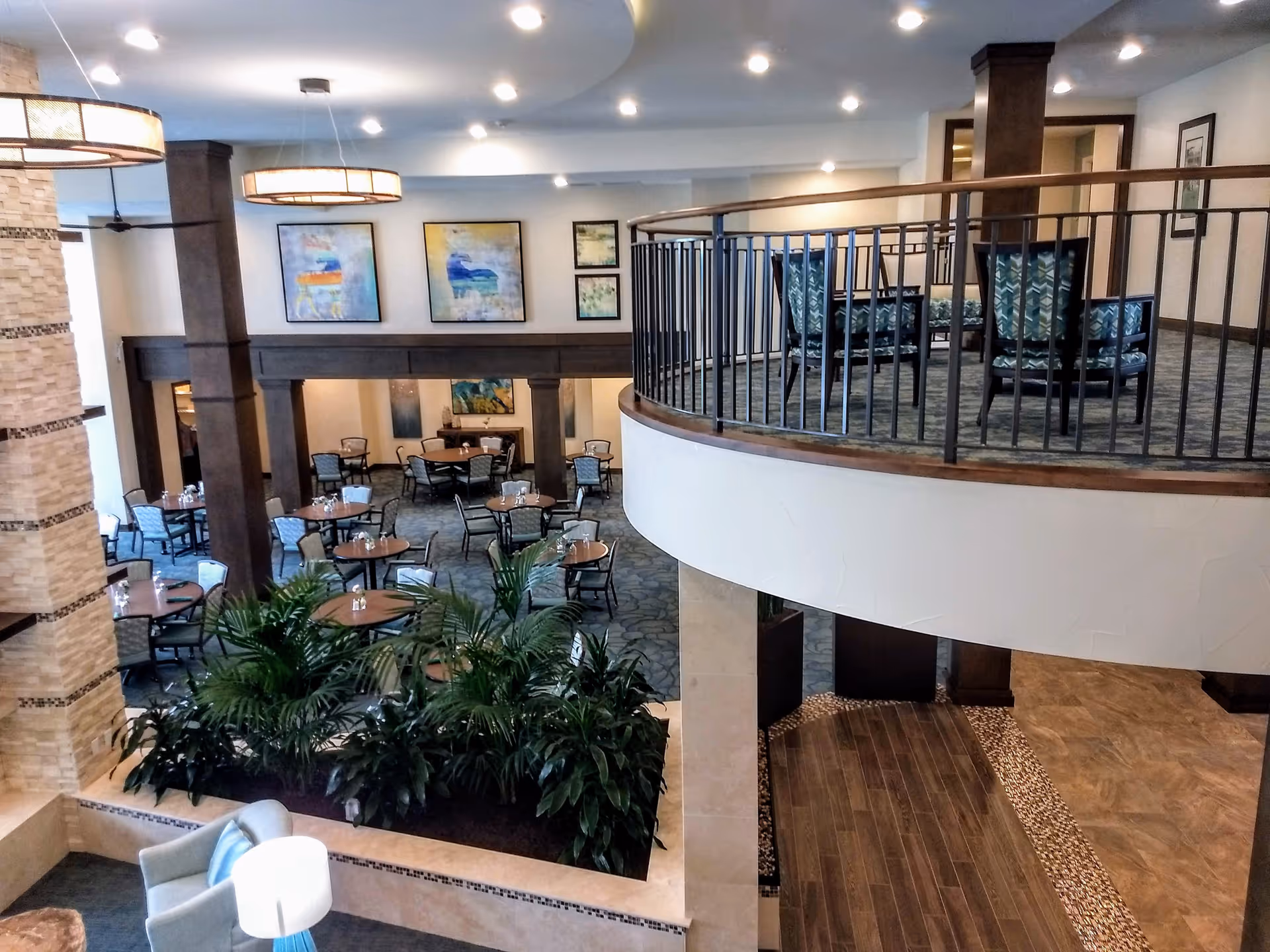 Spacious two-level dining and lounge area with round tables, plants, and an upper balcony seating area.