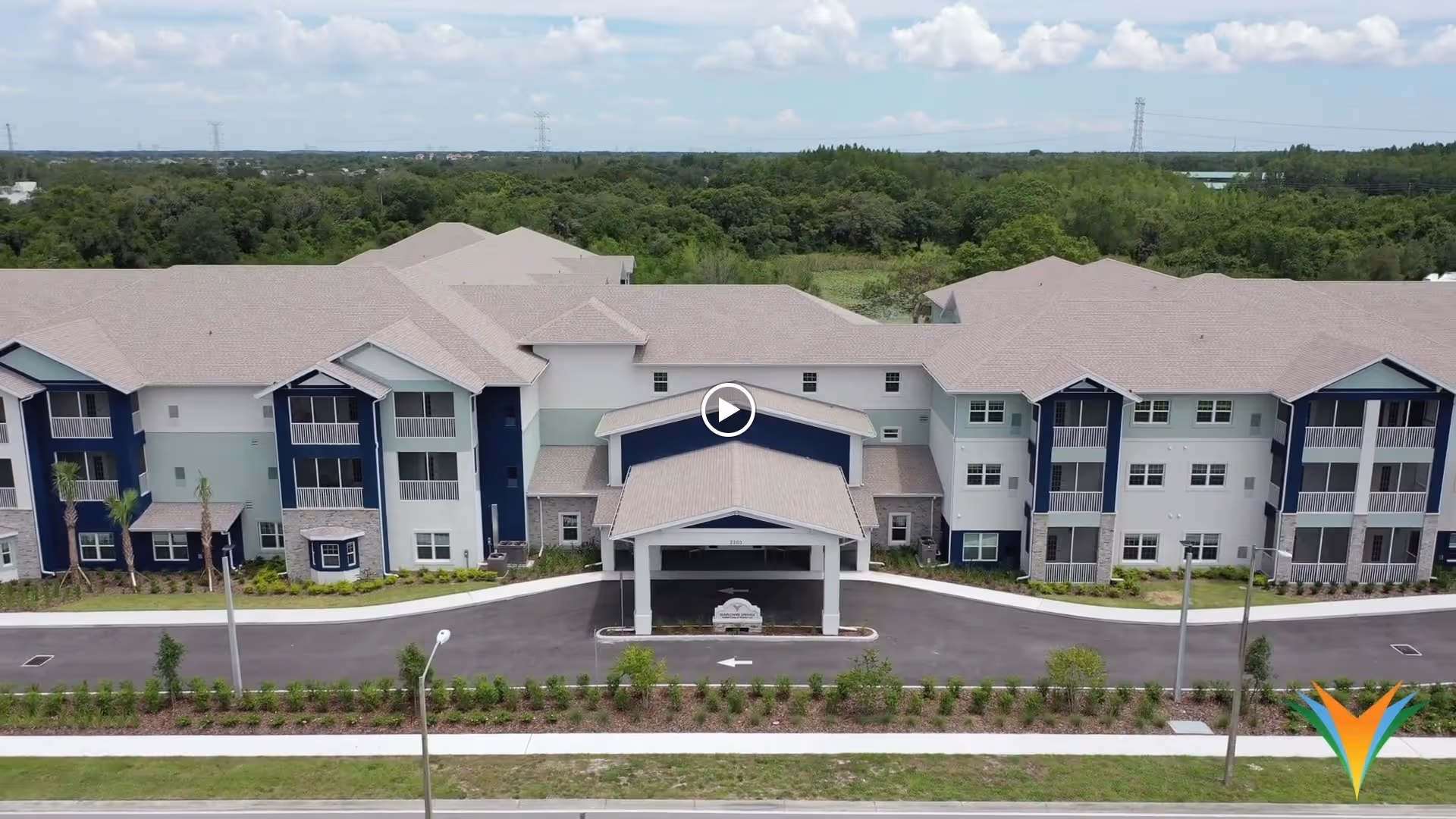 Front exterior of a three-story senior living building with a covered entrance, driveway, and landscaped grounds.