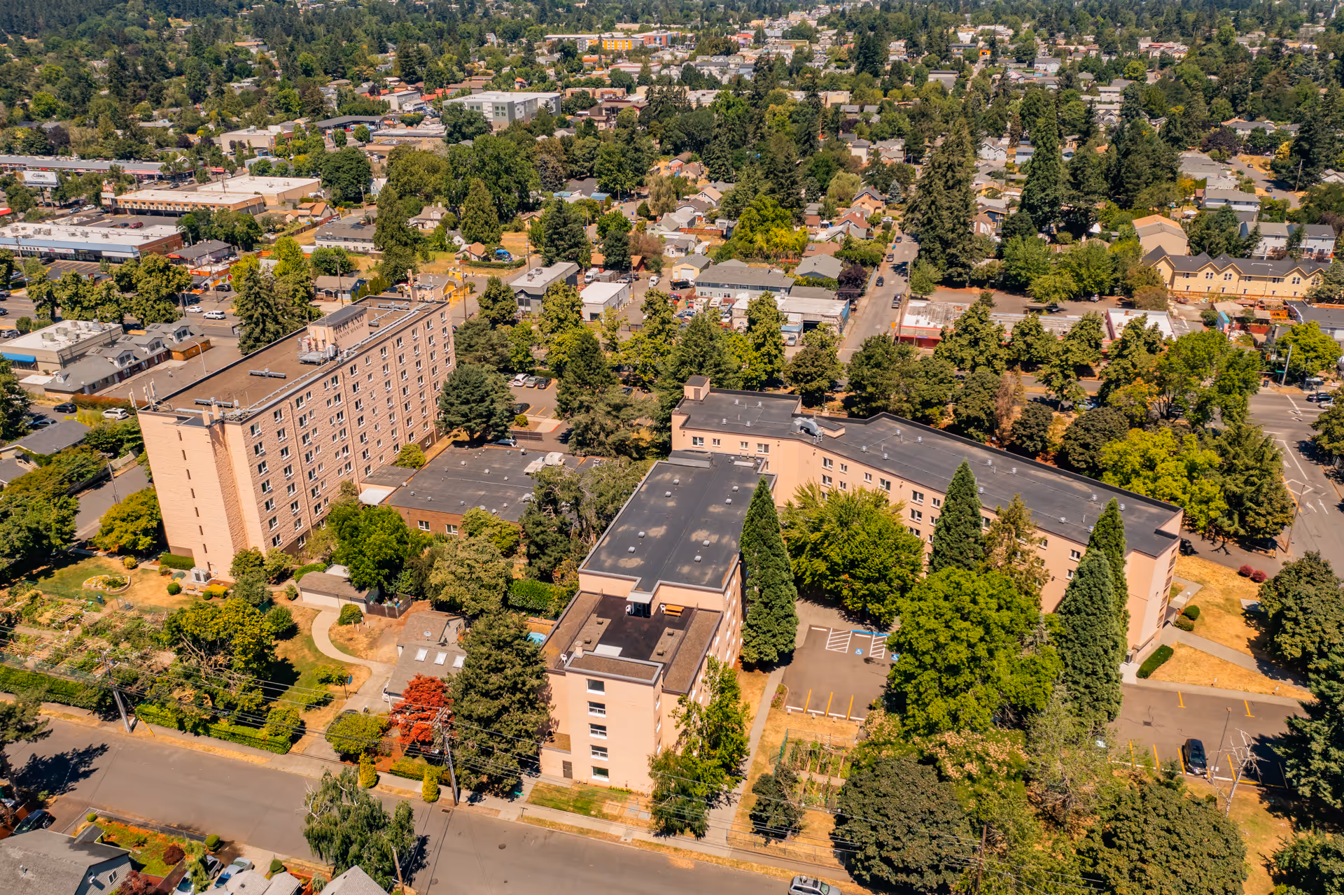 Aerial view of Kirkland Union Manors, showing multiple connected residential buildings surrounded by trees and greenery, with a neighborhood of houses and streets in the background.