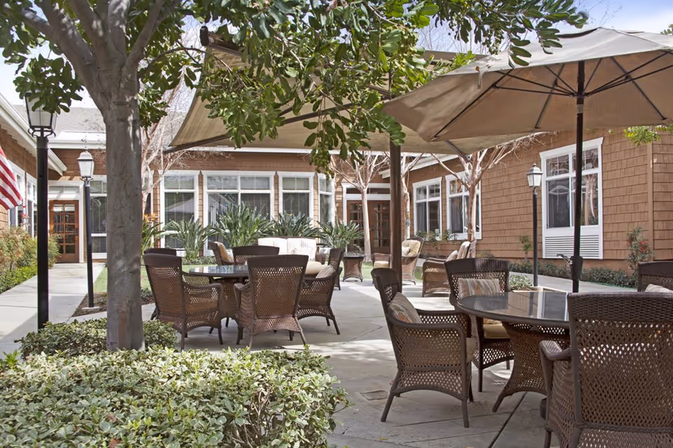 Outdoor courtyard patio with wicker tables and chairs, umbrellas, and surrounding building facades.