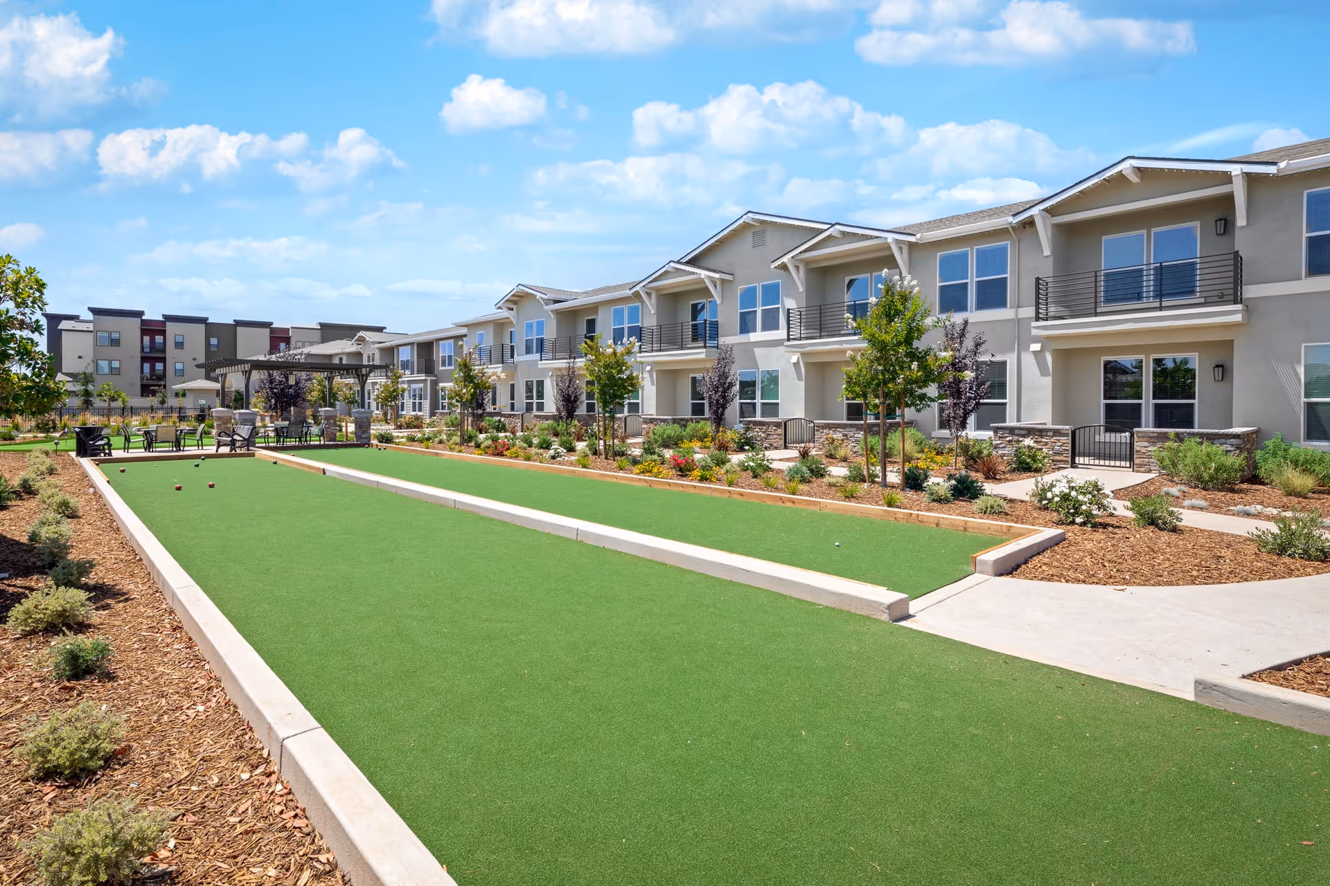 Outdoor bocce court and seating area in front of a two-story senior living apartment building under a blue sky.