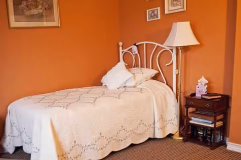 Orange-walled bedroom featuring a white metal bed, lamp, and nightstand.