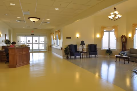 Spacious reception lobby with a front desk on the left, seating area with chairs and a couch on the right, and glass entrance doors straight ahead.