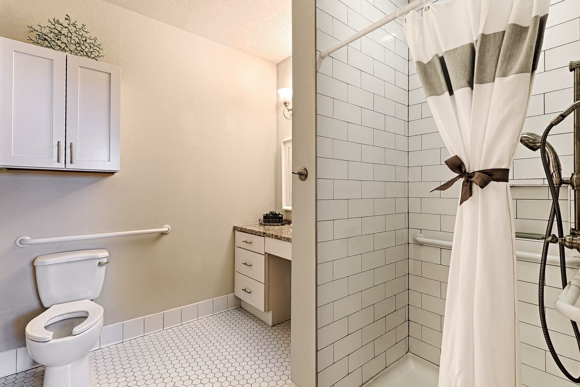 Bright accessible bathroom with a toilet, vanity, grab bars, and a tiled walk-in shower with a tied-back curtain.