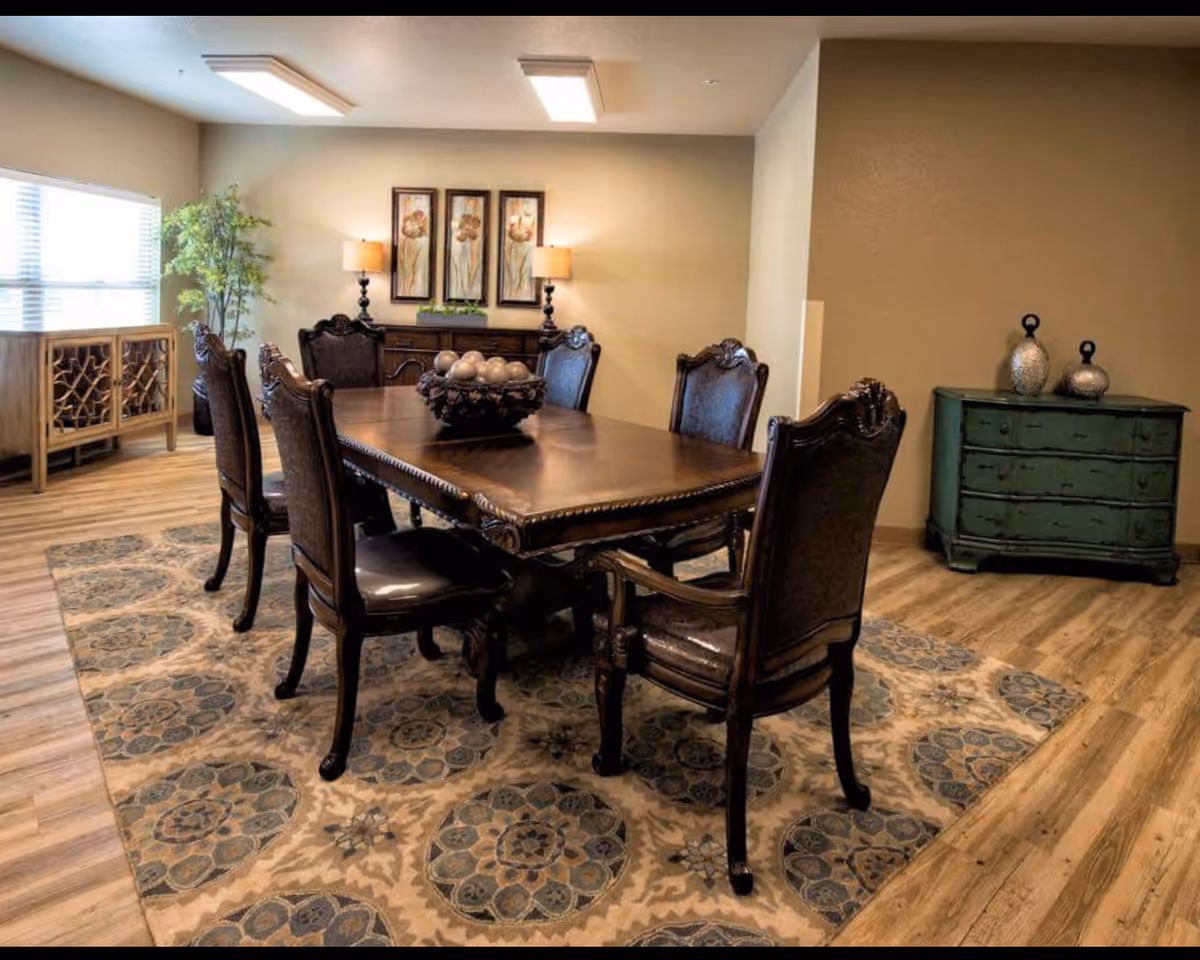 A formal dining room with a dark wood table and ornate chairs on a patterned rug, flanked by cabinets and decorative accents.
