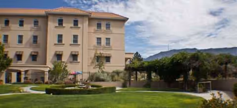 Three-story beige senior living facility with manicured courtyard and distant mountains.