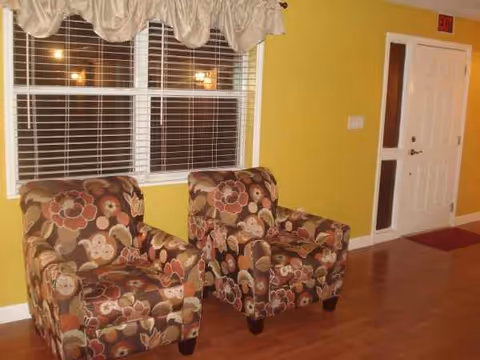Bright yellow living area with floral patterned chairs and large window blinds.