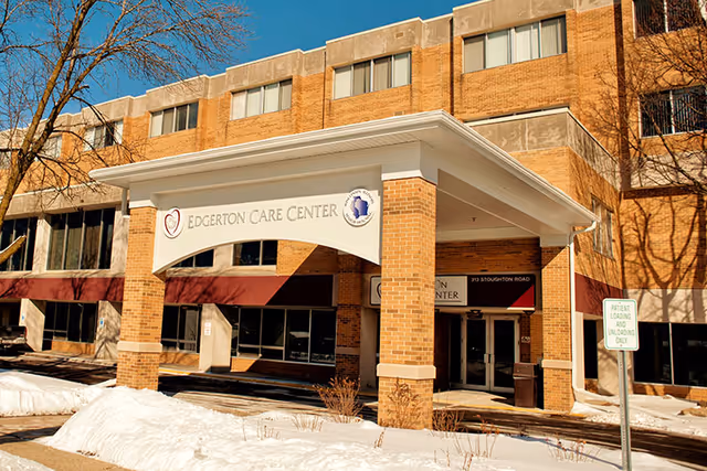 Front entrance of Edgerton Care Center with a covered portico and signage on a brick multi-story building amid snow.