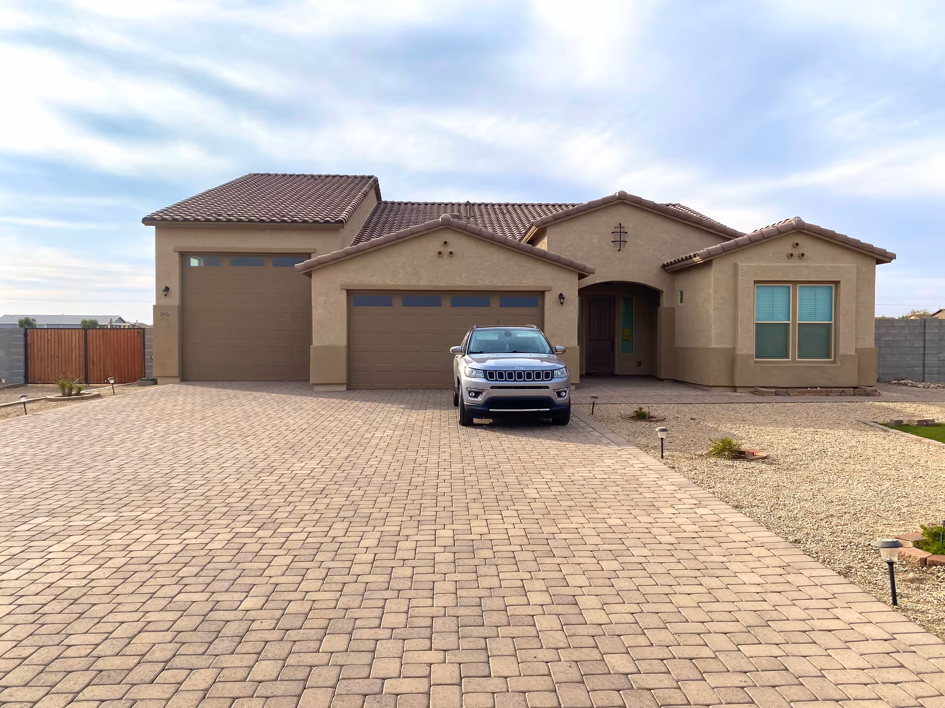 Front view of a beige stucco single-story house with a three-car garage and an SUV parked on a large paved driveway.