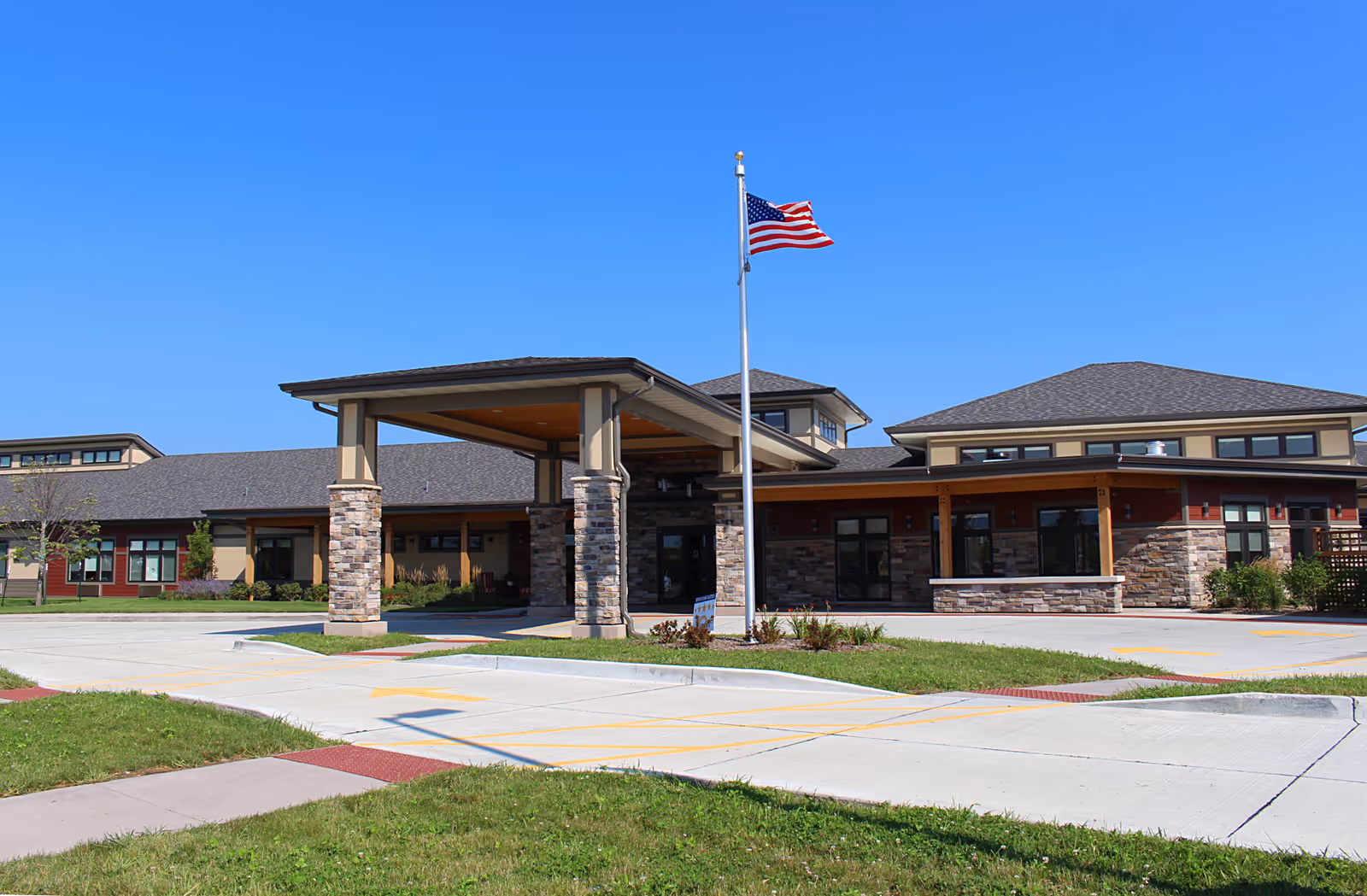 Front exterior of a senior care building with a covered entrance and an American flag on a flagpole.