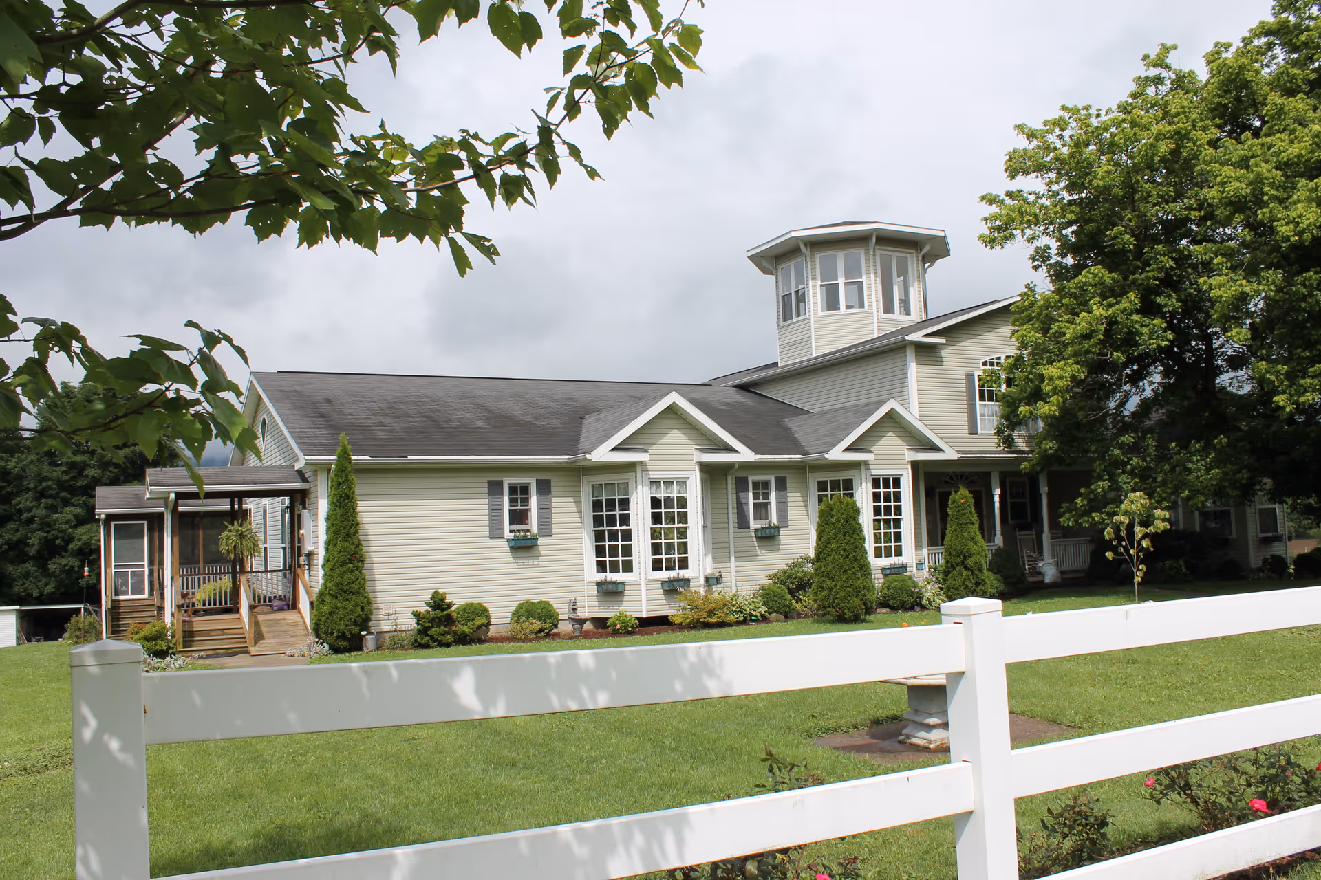 Front view of a light-colored single-story building with a cupola, white fence, and landscaped lawn.