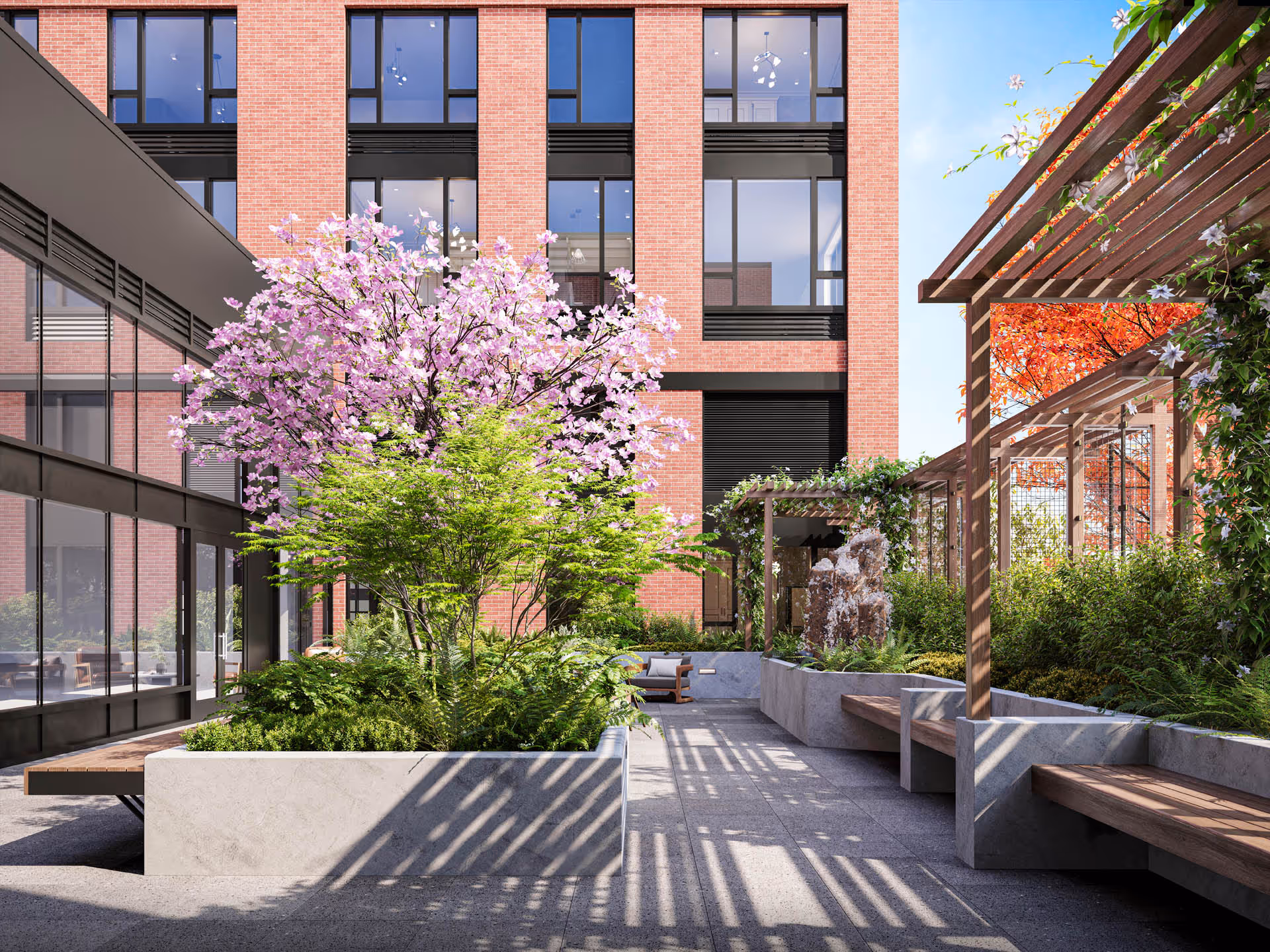 Sunny landscaped courtyard with a flowering pink tree, pergolas, benches, and a brick building in the background.