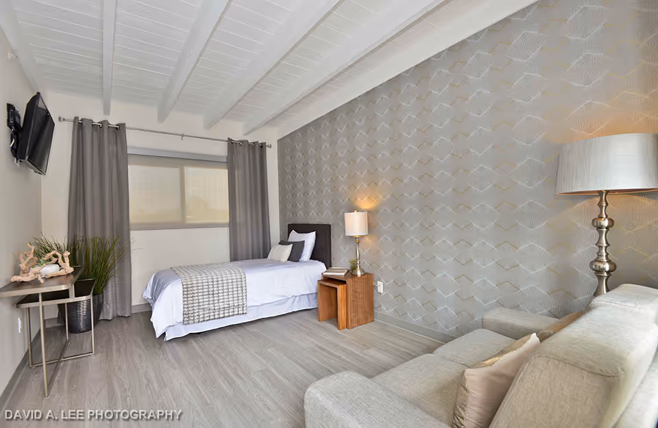 Bright modern bedroom with a single bed, sofa, patterned accent wall, nightstand, lamps and a wall-mounted TV.