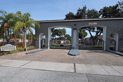 Gated arched entrance to The Villas of Casa Celeste with iron gates, palm trees, and a driveway.