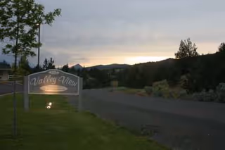 Sunset-lit entrance to Valley View Assisted Living with driveway, sign, and surrounding trees.