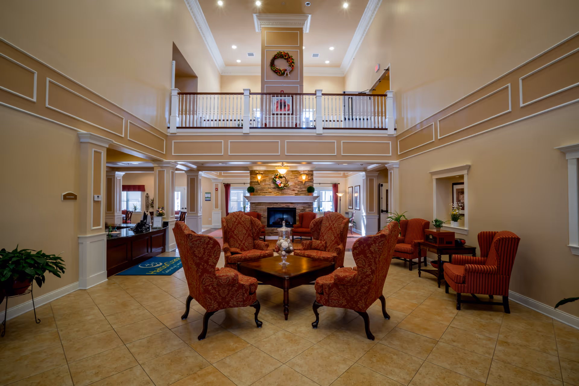 Spacious two-story lobby with a seating group of red upholstered chairs around a central table facing a fireplace and an upper balcony.