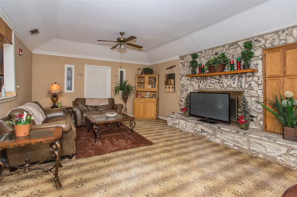 Cozy living room with leather sofas, a coffee table, ceiling fan, and a stone fireplace with a TV and decorative plants.