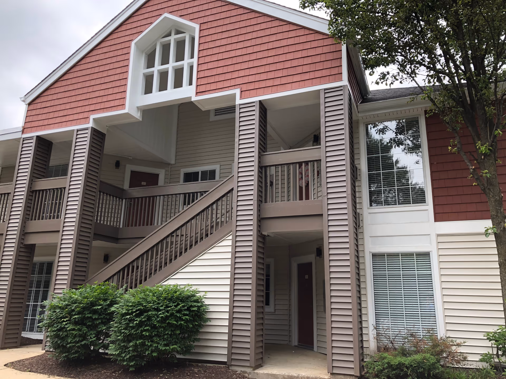 Two-story senior living building exterior with an open stairway, second-floor walkways, entry doors, and shrub landscaping.