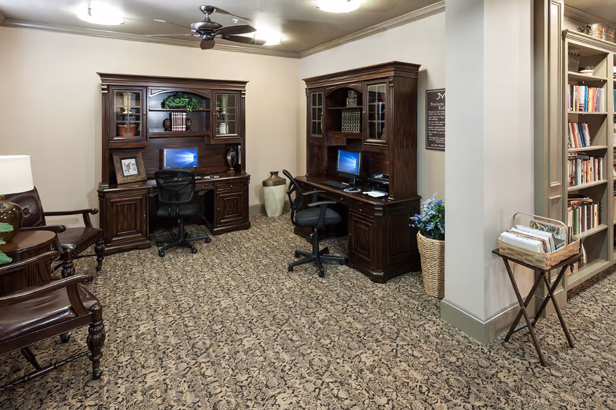 A comfortable business-center/library room with two dark wooden computer desks, office chairs, bookshelves and seating.