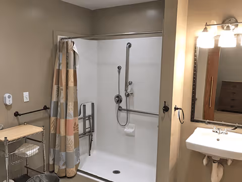 Accessible bathroom with a roll-in shower, grab bars, shower curtain, sink, and mirror.