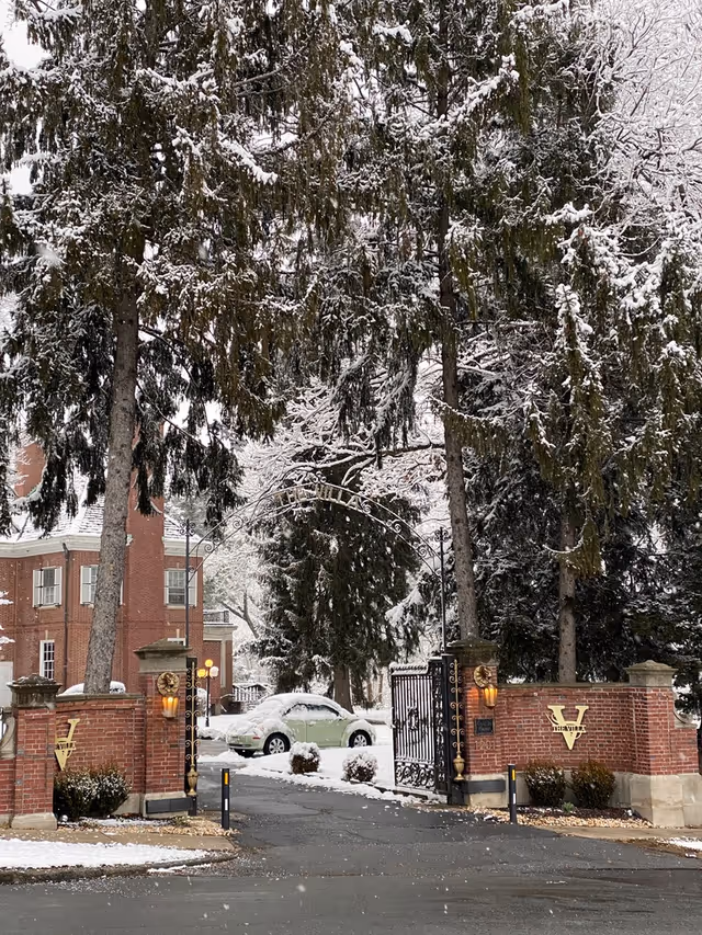 Snowy entrance to a brick senior living villa with iron gates and tall trees.