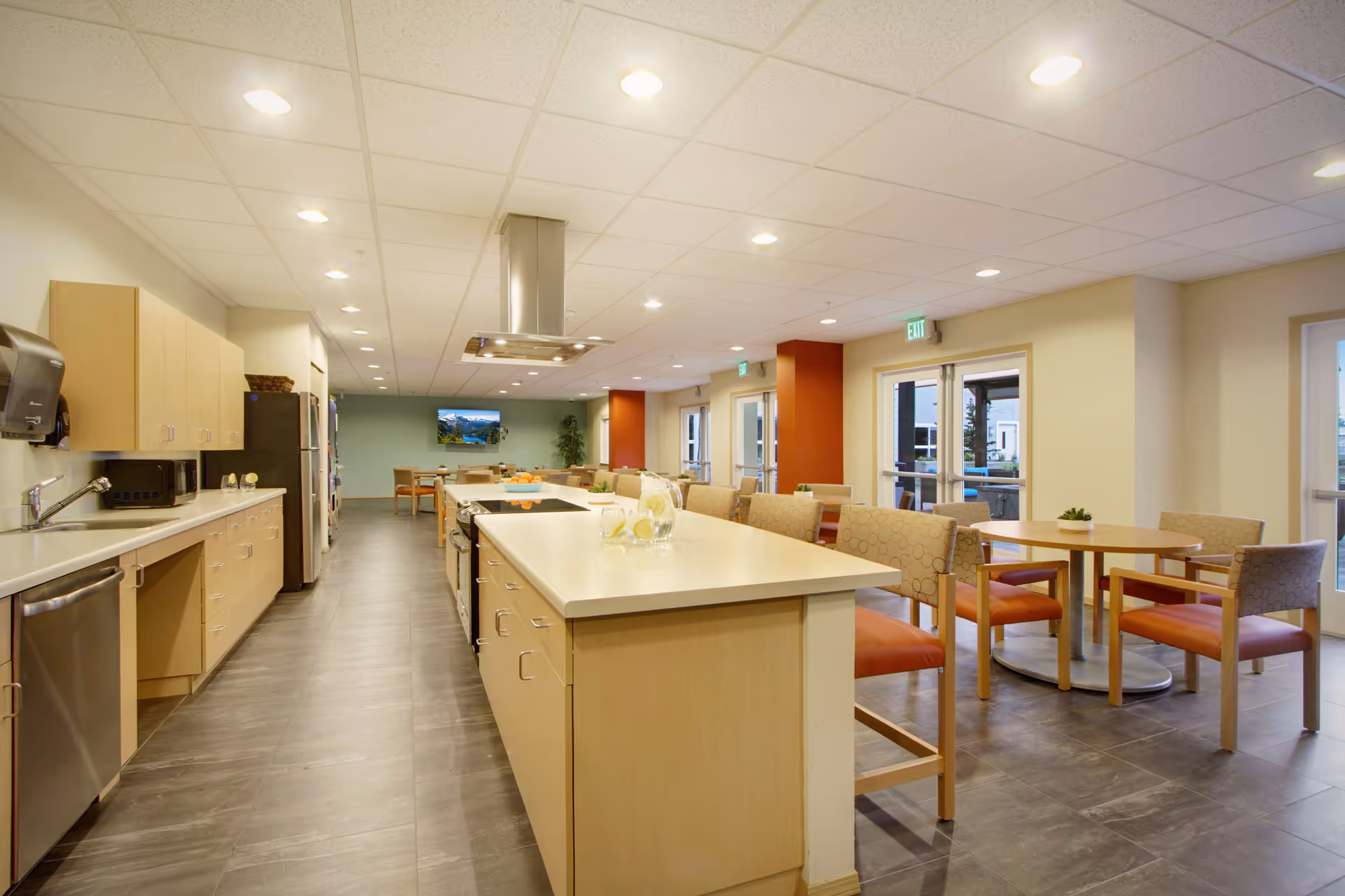 Bright communal kitchen and dining area with a long island, tables, and chairs.