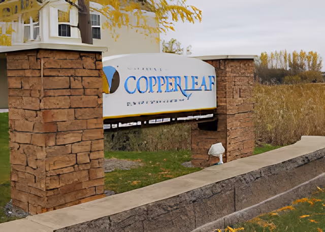 Stone entrance sign reading "Copperleaf" mounted between brick pillars with a building and landscaping behind it.