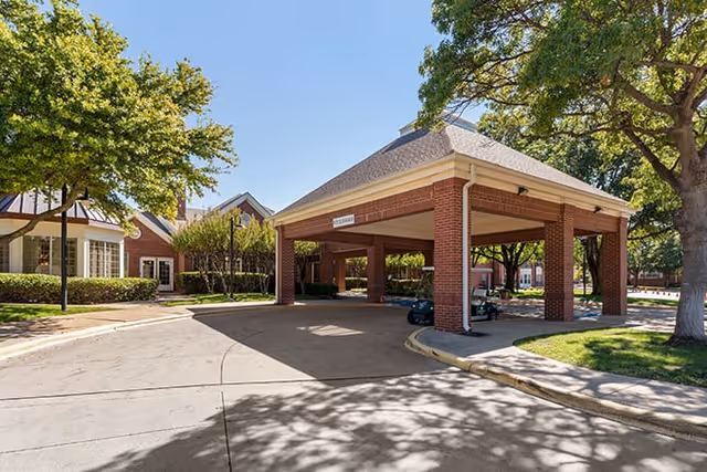 Exterior view of Broadway Cityview facility showing a covered driveway entrance with brick pillars, surrounded by trees and landscaping under a clear blue sky.
