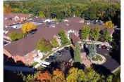 Aerial view of a senior living complex with red-roofed buildings, a circular driveway, parked cars, and trees showing autumn colors.