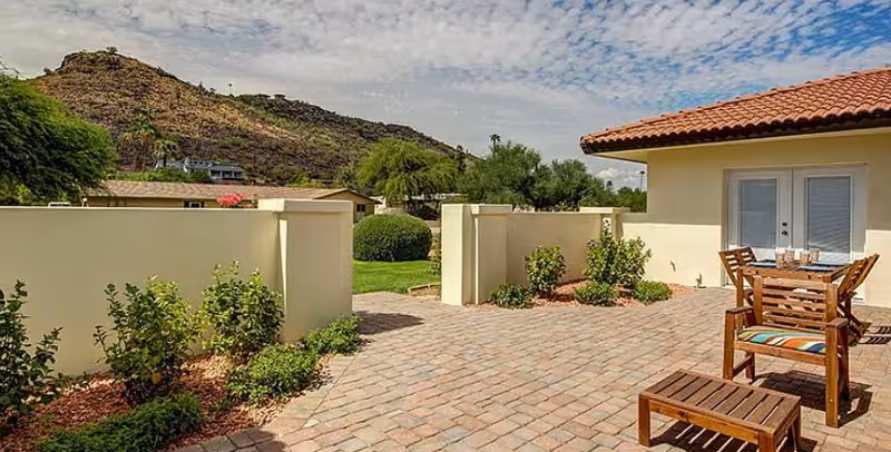 Outdoor patio with brick pavers, wooden furniture, and a beige building with a red-tiled roof.