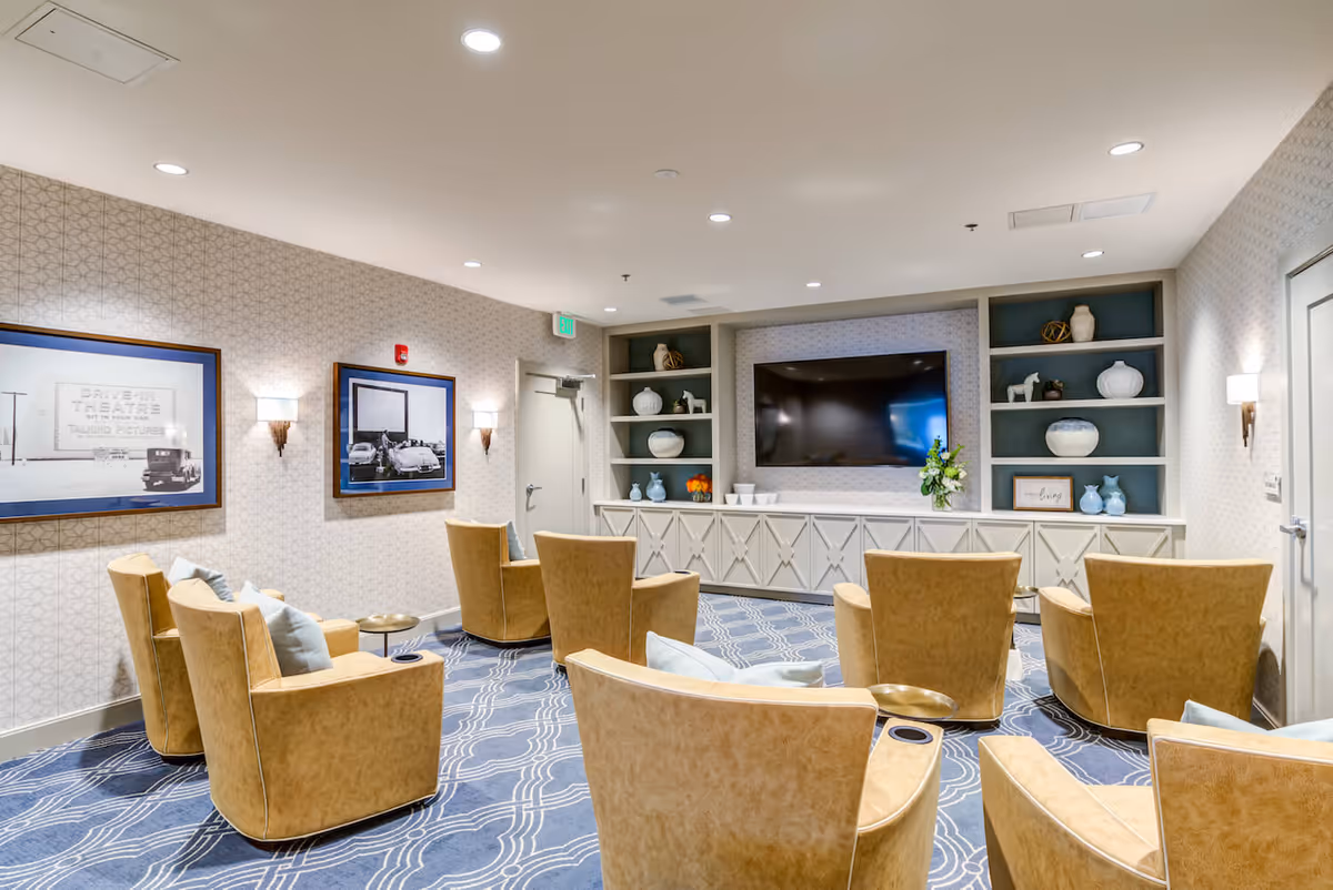 Comfortable TV lounge with tan swivel chairs arranged facing a wall-mounted flat-screen TV and built-in shelving.