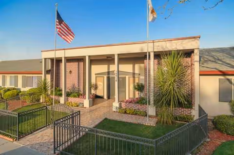 Front view of a brick building entrance with flags and landscaped walkway.