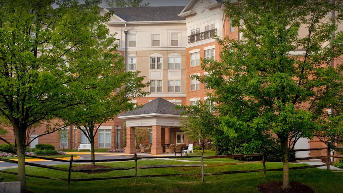 Exterior view of a multi-story senior living building with brick facade and green trees.