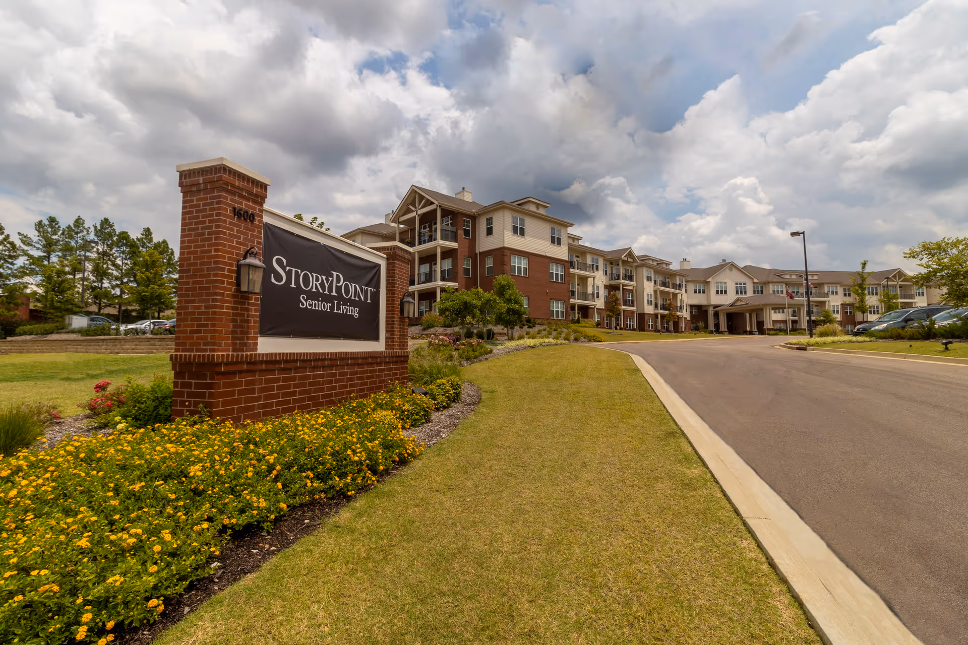 Exterior view of StoryPoint Senior Living facility with a large brick sign in the foreground and a multi-story residential building in the background under a partly cloudy sky.