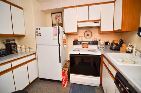 Compact kitchen with white cabinets, a refrigerator, stove, and sink in a senior living facility.