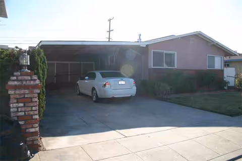 Front exterior of a single-story pink house with a carport and a white sedan.