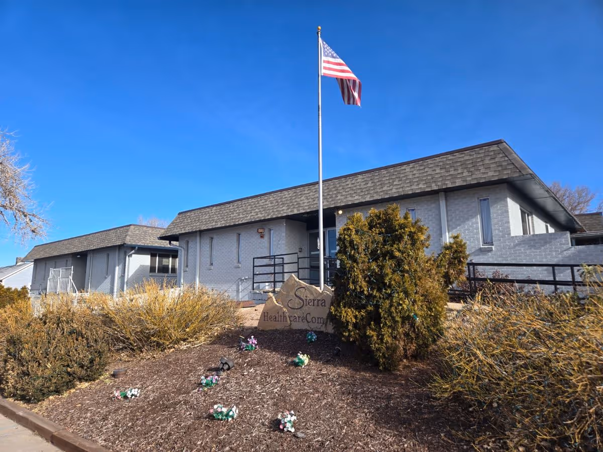Front exterior of a single-story healthcare building with an American flag, landscaped beds, and a stone sign reading 'Sierra'.
