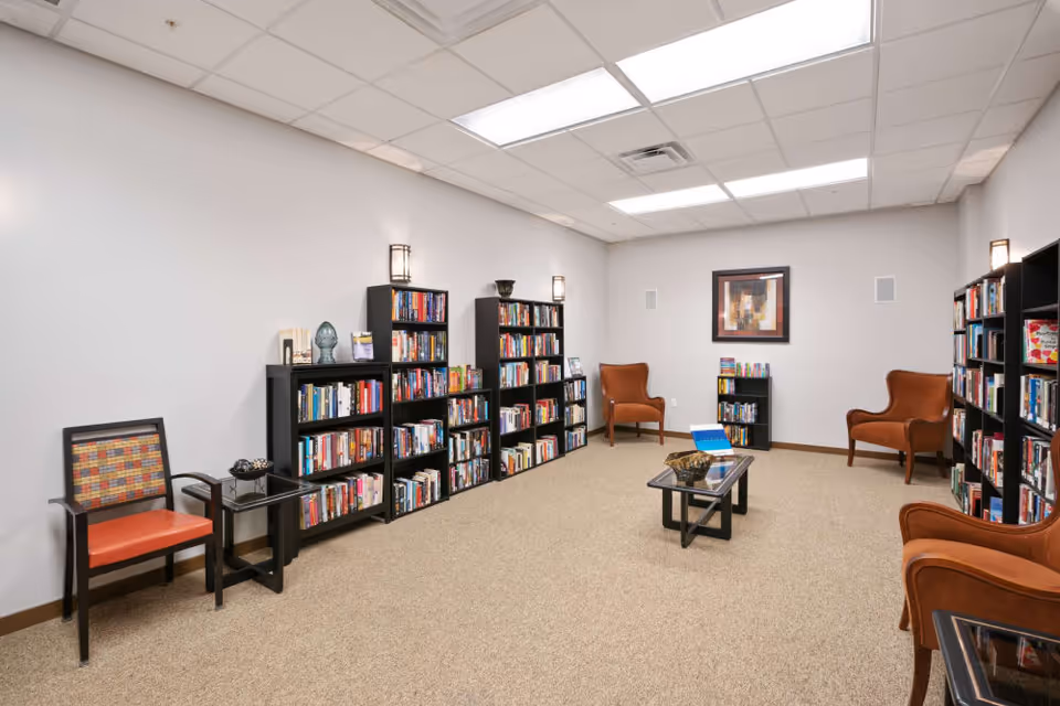 A quiet community reading room with bookshelves along the walls, several armchairs, and a central coffee table.