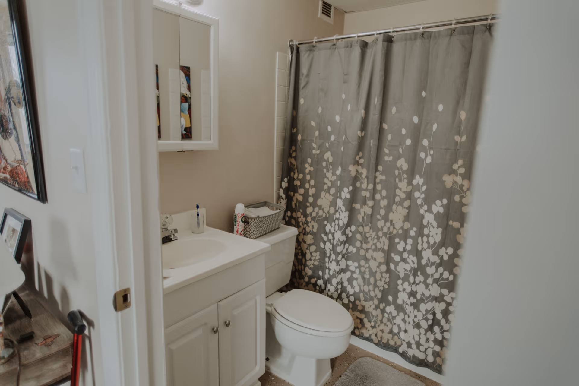 Small bathroom with a white vanity and sink, toilet, and a gray floral shower curtain.